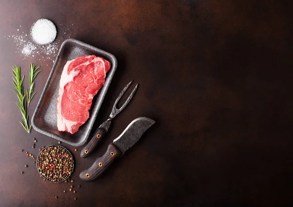 Bife de vaca lombo cru em bandeja de plástico com faca e garfo em fundo enferrujado. Sal e pimenta com alecrim fresco — Fotografia de Stock