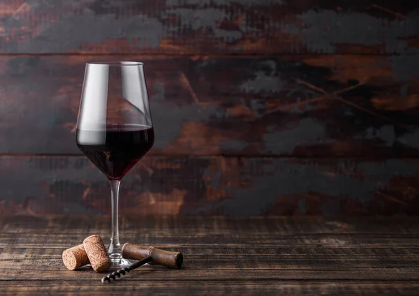Elegant glas rode wijn met kurken en corkscrew op donkere houten achtergrond. Natuurlijk licht — Stockfoto