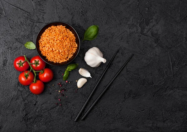 Black plate bowl of rice with tomato and basil and garlic and chopsticks on black stone background. Top view. — Stock Photo, Image