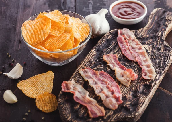 Patatas fritas con sabor backon con rashers de tocino a la parrilla sobre tabla de cortar vintage con ajo y salsa sobre fondo de madera . — Foto de Stock