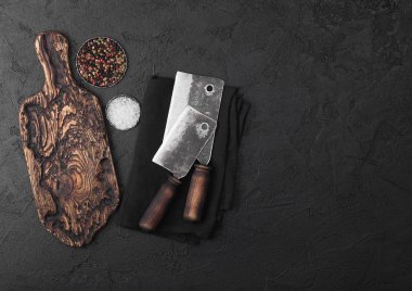 Vintage doğrama tahtası ve siyah taş masa arka plan ile Vintage et bıçağı baltalar. Kasap eşyaları. Tuz ve karabiber. Metin için alan