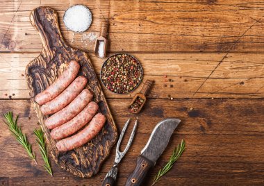 Ahşap arka plan üzerinde vintage bıçak ve çatal ile eski doğrama tahtası üzerinde çiğ sığır eti ve domuz sosis. Biberiyeli tuz ve karabiber. Metin için alan