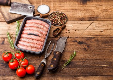 Ahşap arka plan üzerinde vintage bıçak ve çatal ile plastik tepside çiğ sığır eti ve domuz sosis. Tuz ve biber, domates, biberiye ve eski balta. Metin için alan