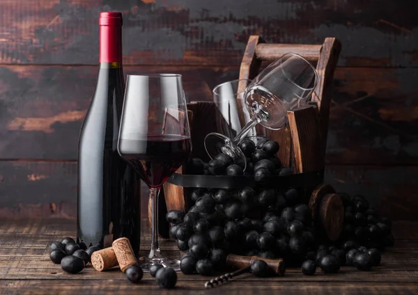 エレガントなガラスと赤ワインのボトルと暗い木製の背景にヴィンテージの木製の樽の中に暗いブドウ。自然光 — ストック写真