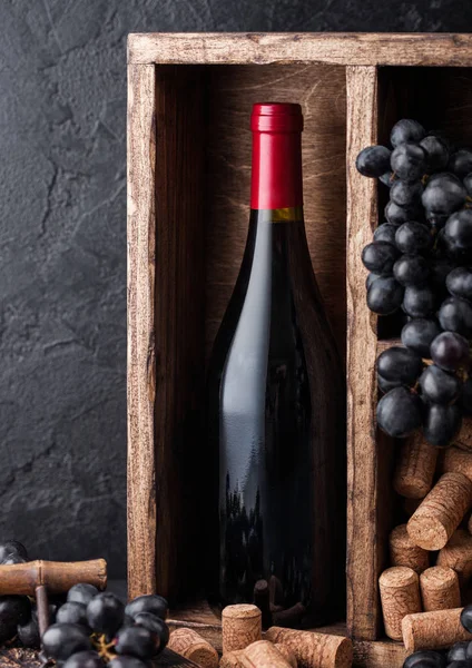 Bottle of red wine with dark grapes and corks inside vintage wooden box on black stone background. Natural Light — Stock Photo, Image