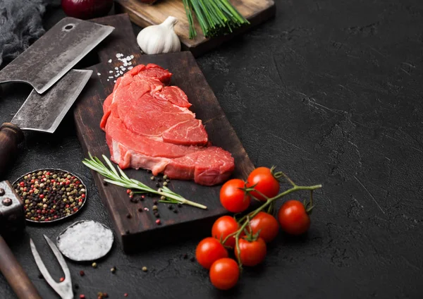 Fresh raw organic slice of braising steak fillet on chopping board with fork and knife on black stone background. Red onion, tomatoes with salt and pepper. Space for text — Stock Photo, Image