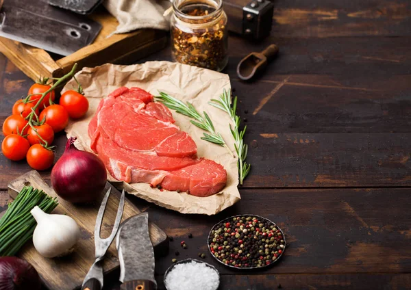 Čerstvý surový organický řez dušené bifteky na řezníky s vidličkou a nožem na tmavém dřevěném pozadí. Červenou cibuli, rajčata se solí a pepřem. Místo pro text — Stock fotografie