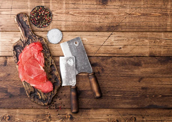 Fatia orgânica crua fresca de filé de bife refogado em tábua de cortar com hatchets de carne em fundo de madeira. Sal e Pimenta — Fotografia de Stock