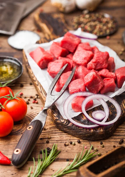Ωμό άπαχο κατσαρόλα σε κύβους βοδινό χοιρινή μπριζόλα με τσεκούρι εκλεκτής ποιότητας κρέας και το μαχαίρι και το πιρούνι σε ξύλινο υπόβαθρο. Αλάτι και πιπέρι με δενδρολίβανο φρέσκο, κόκκινο κρεμμύδι και σκόρδο με δεντρολίβανο — Φωτογραφία Αρχείου