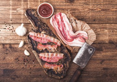 Sarımsak ile ahşap tahta üzerinde et balta ile kasaplar kağıt üzerinde çiğ taze füme domuz pastırması ile vintage ahşap tahta üzerinde Izgara pastırma şeritler.