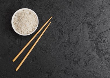 Siyah taş arka planda siyah Chopsticks ile haşlanmış organik Basmati Yasemin pirinç ile beyaz kase. Metin alanı