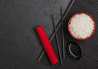 Siyah Chopsticks ve siyah taş arka planda kırmızı keten havlu ile bambu placemat üzerinde tatlı soya sosu ile haşlanmış organik Basmati Yasemin pirinç ile kırmızı kase. Metin alanı