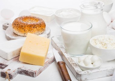 Beyaz masa artalanını vintage ahşap kutusunda taze süt ürünleri. Kavanoz ve süt, kase ekşi krema, peynir ve yumurta. Taze pişmiş yemiyorsun yuvarlak bıçak ile kesme tahtası.
