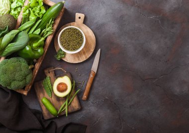 Koyu arka plan üzerinde ahşap kutu içinde çeşitli yeşil tonda çiğ organik sebze. Avokado, lahana, karnabahar ve salatalık kesilmiş ve mung fasulye ve bıçak ile doğrama tahtası ile. Metin için alan