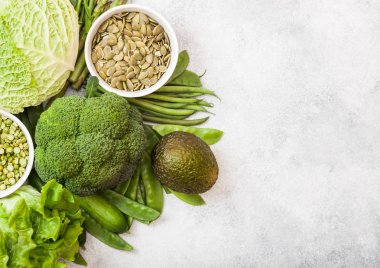 Beyaz arka plan üzerinde çeşitli yeşil tonda çiğ organik sebze. Avokado, lahana, brokoli, karnabahar ve salatalık ile kesilmiş fasulye ve beyaz kase pumkin tohumları.