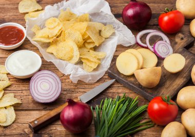 Taze organik ev yapımı patates cips ekşi krema ve kırmızı soğan ve baharat ahşap arka plan üzerinde cips. Doğrama tahtasında taze sarı patates ile.