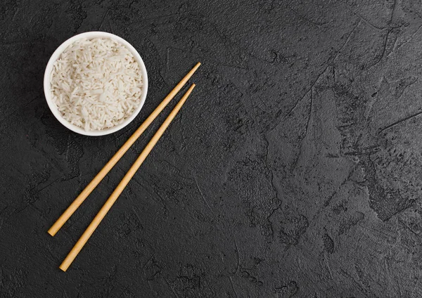 Siyah taş arka planda siyah Chopsticks ile haşlanmış organik Basmati Yasemin pirinç ile beyaz kase. Metin alanı