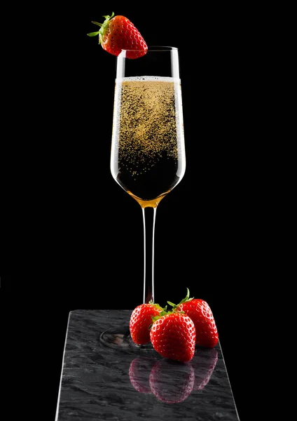 Copo elegante de champanhe amarelo com morango em cima e bagas frescas na placa de mármore preto no fundo preto . — Fotografia de Stock
