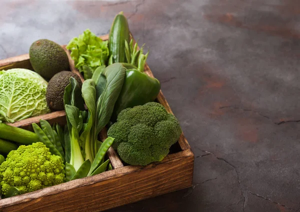 Assorted green toned raw organic vegetables in wooden box on dark background. Avocado, cabbage, cauliflower and cucumber with trimmed and mung beans and pepper and broccoli with sparagus tips. — Stock Photo, Image