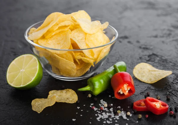 Prato tigela de vidro com batatas fritas batatas fritas com sabor de cebola no fundo da mesa de pedra preta. Pimentos de pimenta vermelha e verde com limão e molho picante quente . — Fotografia de Stock