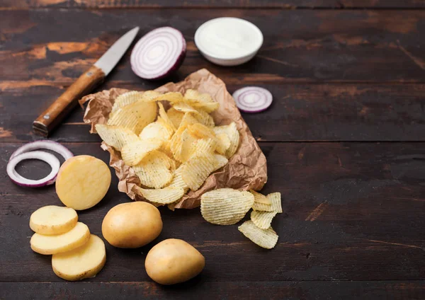 Patatas fritas frescas orgánicas caseras con crema agria y cebollas rojas sobre papel sobre fondo de madera oscura . — Foto de Stock