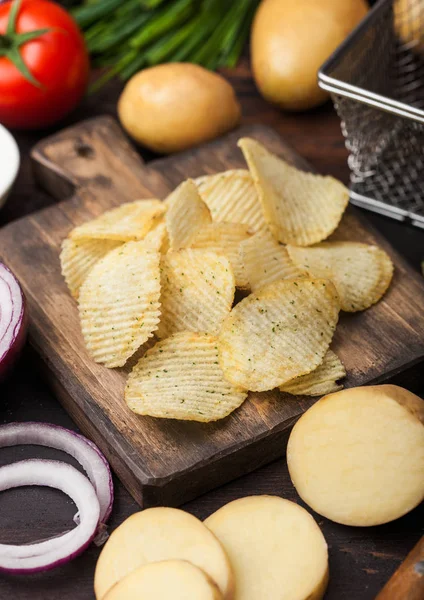 Patatas fritas frescas orgánicas caseras con crema agria y cebollas rojas sobre tabla de cortar sobre fondo de madera oscura. Tomates con cebolla verde y tazón de ketchup . — Foto de Stock