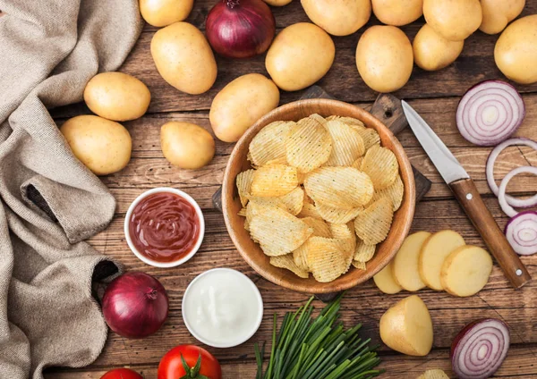Fresh organic homemade potato crisps chips in wooden bowl with sour cream and red onions and spices on wooden table background. Top view.Fresh yellow potatoes with ketchup — Stock Photo, Image