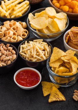 Fıstık, patlamış mısır ve soğan halkaları ve siyah arka planda kase plakaları tuzlu kraker ile tüm klasik patates atıştırmalıkları. Cips ve patates cipsi, nachos ve peynir topları ile cipsler ile Twirls.