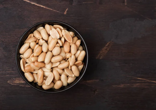 Salted and roasted peanuts classic snack in black bowl on wooden background. — Stock Photo, Image