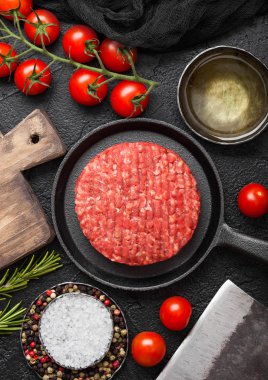 Taze çiğ kıyılmış ev yapımı çiftçiler yuvarlak Doğrama Kurulu ve baharat ve otlar ve siyah tahta et balta ile tava tava üzerinde sığır Burger ızgara. Yağ, sarımsak ve domates.
