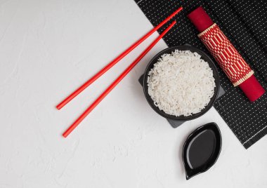 Siyah taş arka plan üzerinde kırmızı keten havlu ile bambu placemat üzerinde kırmızı çubuklar ve tatlı soya sosu ile haşlanmış organik basmati yasemin pirinç ile Siyah kase. Metin için alan