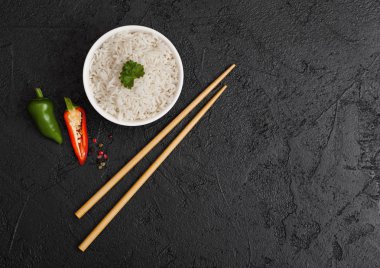 Kaynamış organik basmati yasemin pilavlı beyaz kase. Siyah çubuklu siyah yemek çubuğu, yeşil ve kırmızı biberli. Metin için boşluk