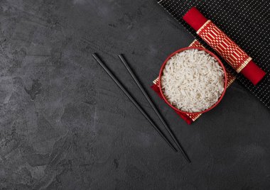 Siyah taş arka plan üzerinde kırmızı keten havlu ile bambu placemat üzerinde siyah çubuklar ile haşlanmış organik basmati yasemin pirinç ile Kırmızı kase. Metin için alan