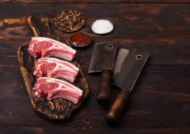 Ahşap arka plan üzerinde vintage et baltalar ile doğrama tahtası taze çiğ kasaplar kuzu sığır pirzola. Çelik kasede tuz, karabiber ve yağ. 