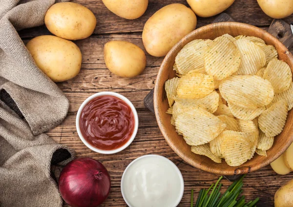 Patatas fritas frescas orgánicas hechas en casa en un tazón de madera con crema agria y cebollas rojas y especias sobre fondo de mesa de madera. Vista superiorPatatas amarillas frescas con salsa de tomate — Foto de Stock