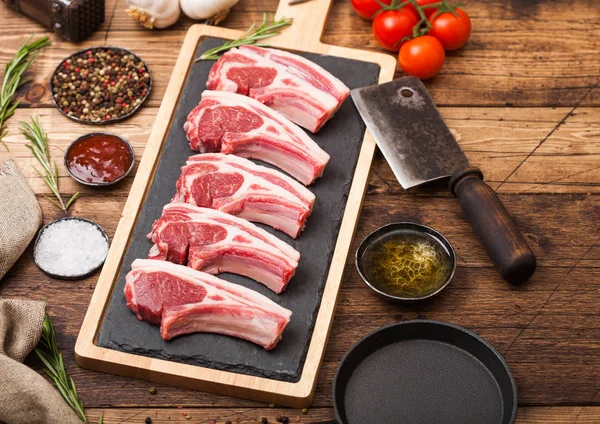 Carniceiros crus frescos costeletas de carne de cordeiro em tábua de corte com machado de carne vintage e martelo em fundo de madeira.Sal, pimenta e óleo com tomate e alho e molho de churrasco . — Fotografia de Stock