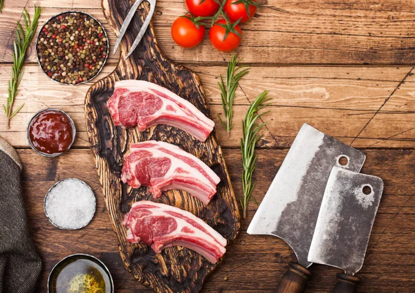 Fresh raw butchers lamb beef cutlets on chopping board with vintage meat hatchets on wooden background.Salt, pepper and oil with tomatoes and garlic and barbeque sauce and fork — Stock Photo, Image