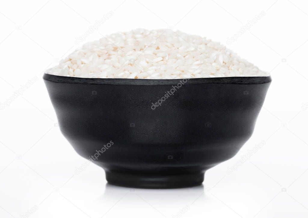 Black bowl of raw organic arborio risotto rice on white background. Healthy food. 