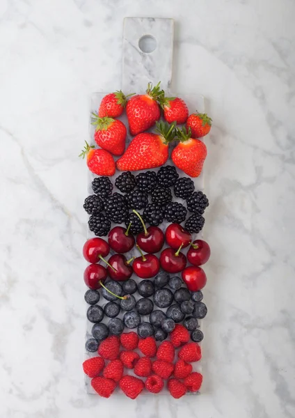Fresh organic summer berries mix on white marble board on marble background. Raspberries, strawberries, blueberries, blackberries and cherries.