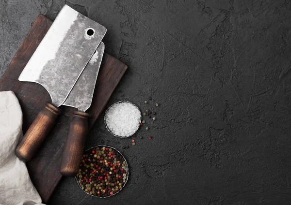 Hacha de cuchillo de carne vintage sobre tabla de cortar vintage y fondo de mesa de piedra negra. Utensilios de carnicero. Sal y pimienta . — Foto de Stock