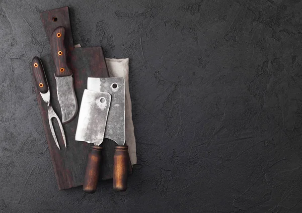 Vintage maso nůž a vidličku a sekery s vintage prkýnko a černý stůl pozadím. Řezník nádobí. Prostor pro text — Stock fotografie
