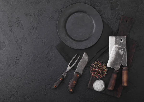 老式肉刀叉和斧头与老式切菜板和板在黑色的桌子背景。屠夫用具。文本的空间 — 图库照片