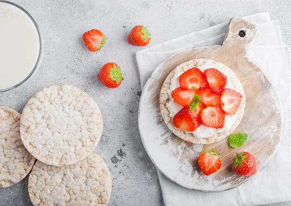 Healthy organic rice cakes with ricotta and fresh strawberries and glass of milk on light stone kitchen background. Top view