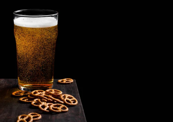 Стакан пива с крендельками на винтажной деревянной доске на черном фоне. Пиво и закуска. Пространство для текста — стоковое фото