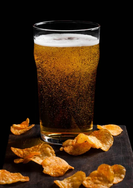 Vaso de cerveza lager con patatas fritas snack en tablero de madera vintage sobre fondo negro. Cerveza y merienda . — Foto de Stock