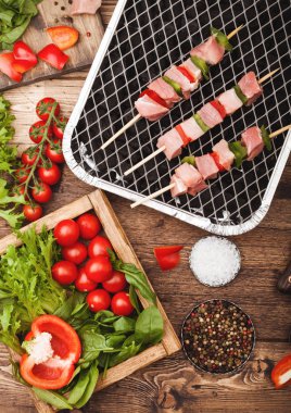 Çatal ve bıçak ile ahşap arka planda taze sebzeler ile tek kullanımlık kömür BBQ ızgara üzerinde Paprika ile ham domuz kebap. Tuz ve biber ile marul ve Paprika ve kiraz domates. Üst görünüm
