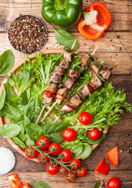 Domates ve ıspanak ile ahşap arka planda, marul salatası yuvarlak ahşap plaka içinde Paprika ile ızgara domuz ve tavuk kebap. Makro