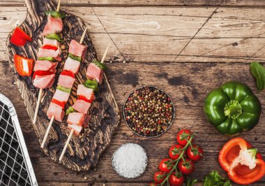 Çatal ve bıçak ile ahşap arka planda taze sebzeler ve tek kullanımlık kömür ızgara ile doğrama tahtasında Paprika ile ham domuz kebap. Tuz ve biber, marul ve Paprika. Üst görünüm