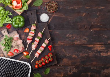 Çatal ve bıçak ile ahşap arka planda taze sebzeler ve tek kullanımlık kömür ızgara ile doğrama tahtasında Paprika ile ham domuz kebap. Tuz ve biber, marul. Metin alanı