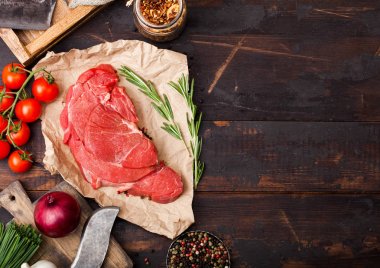 Koyu ahşap arka plan üzerinde çatal ve bıçak ile kasaplar kağıt üzerinde braising biftek fileto Taze ham organik dilim. Kırmızı soğan, tuz ve biberli domates. Metin için alan